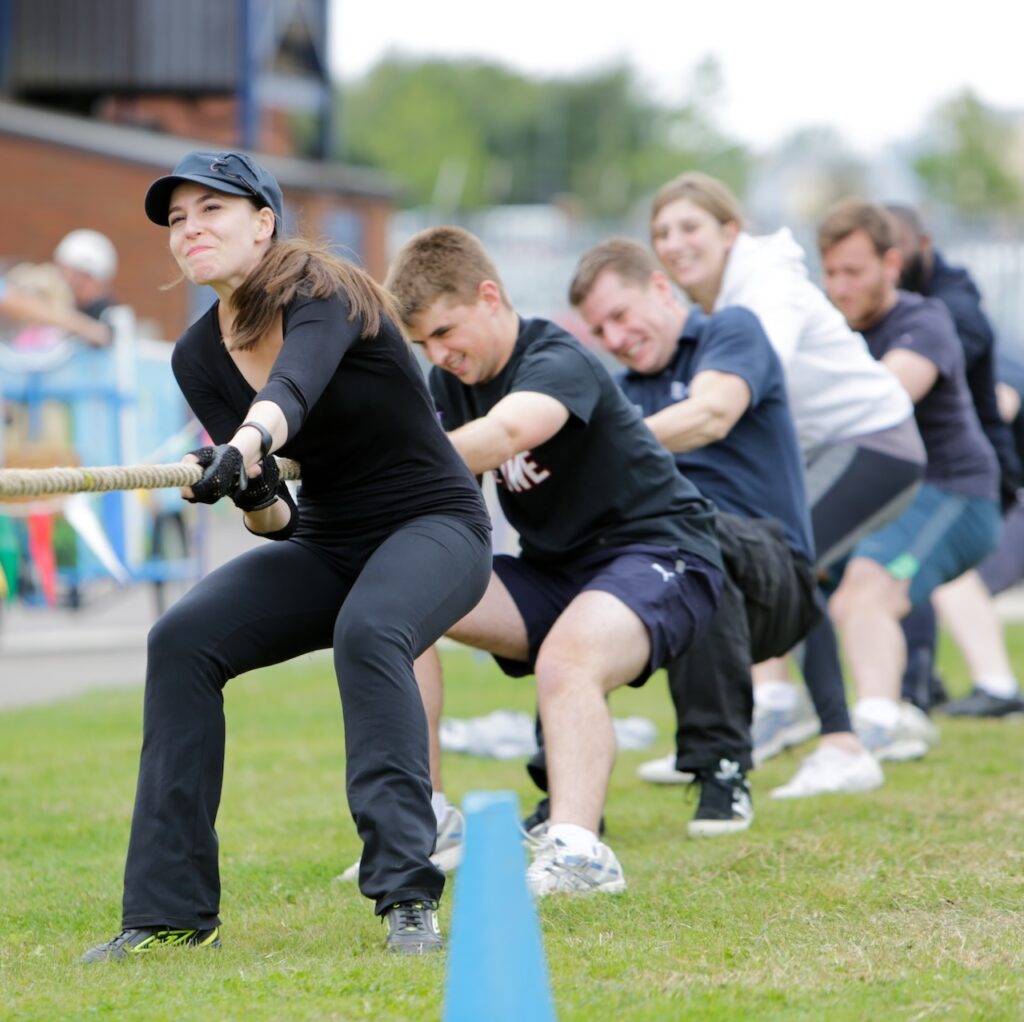 A tug of war team in action, lead by a woman wearing a black cap.